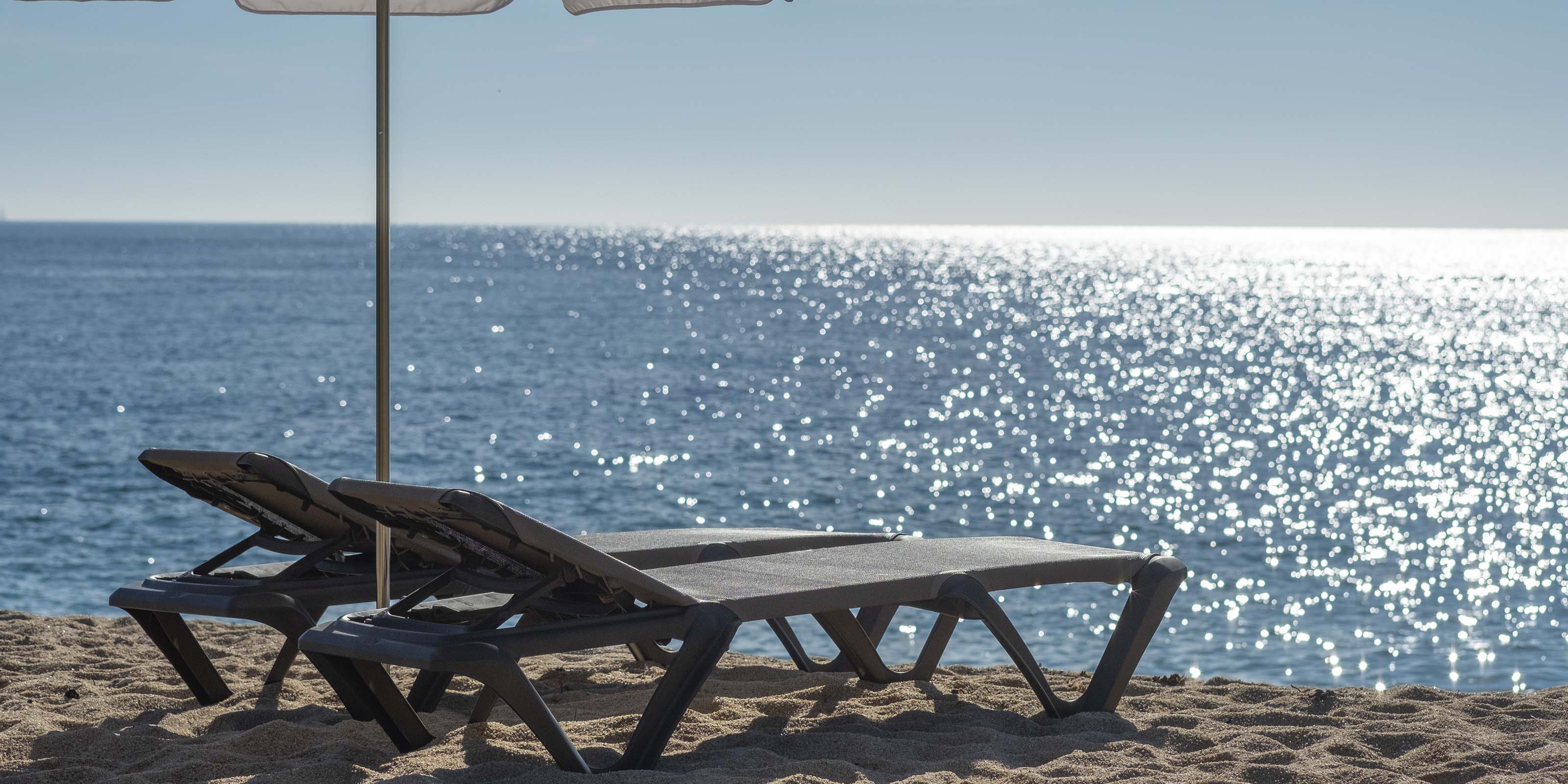 Two Chaise Lounges on a beach overlooking the ocean with a sunset on the horizon