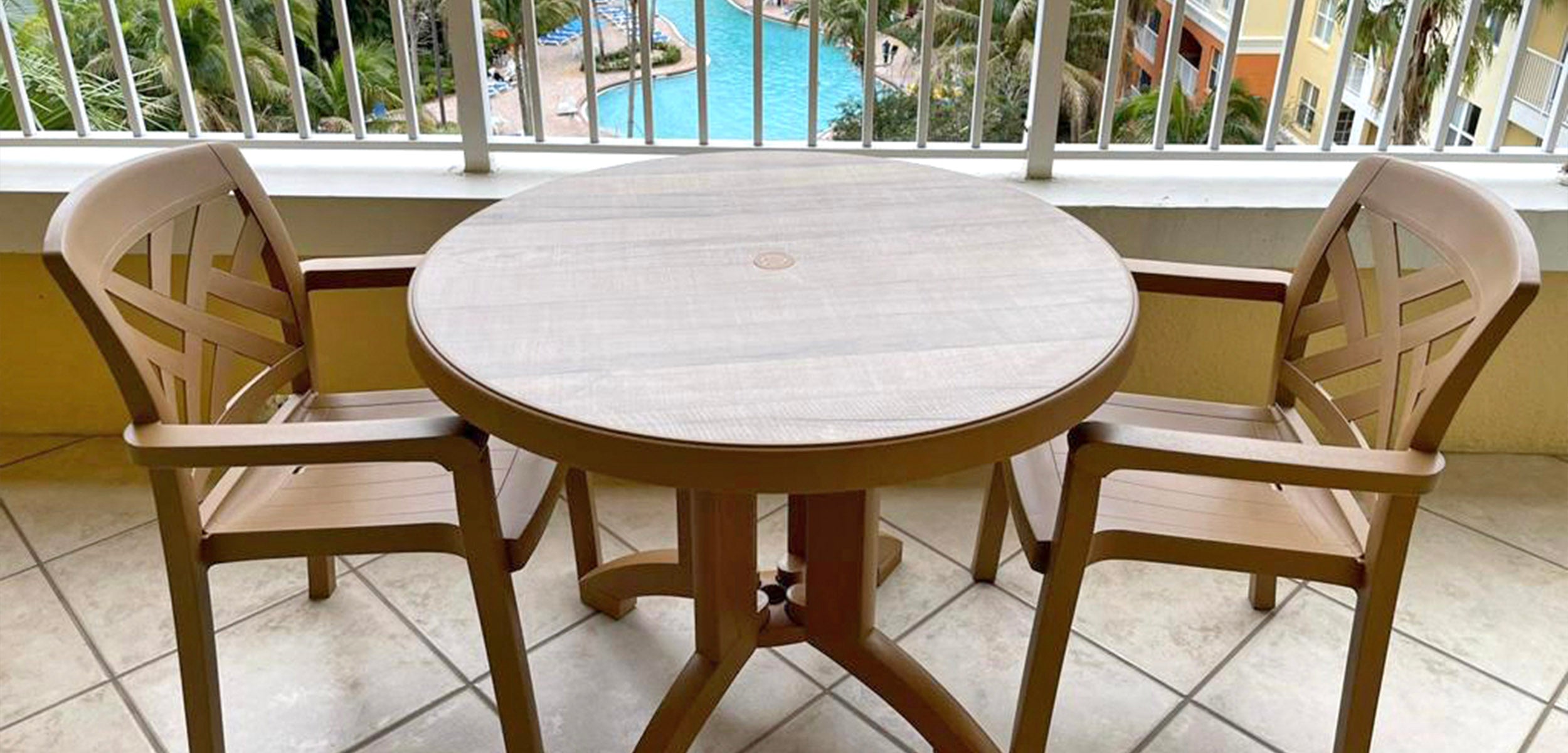 A Grosfillex Aquaba Table and Sanibel Armchairs overlook the pool on the balcony at Vacation Village