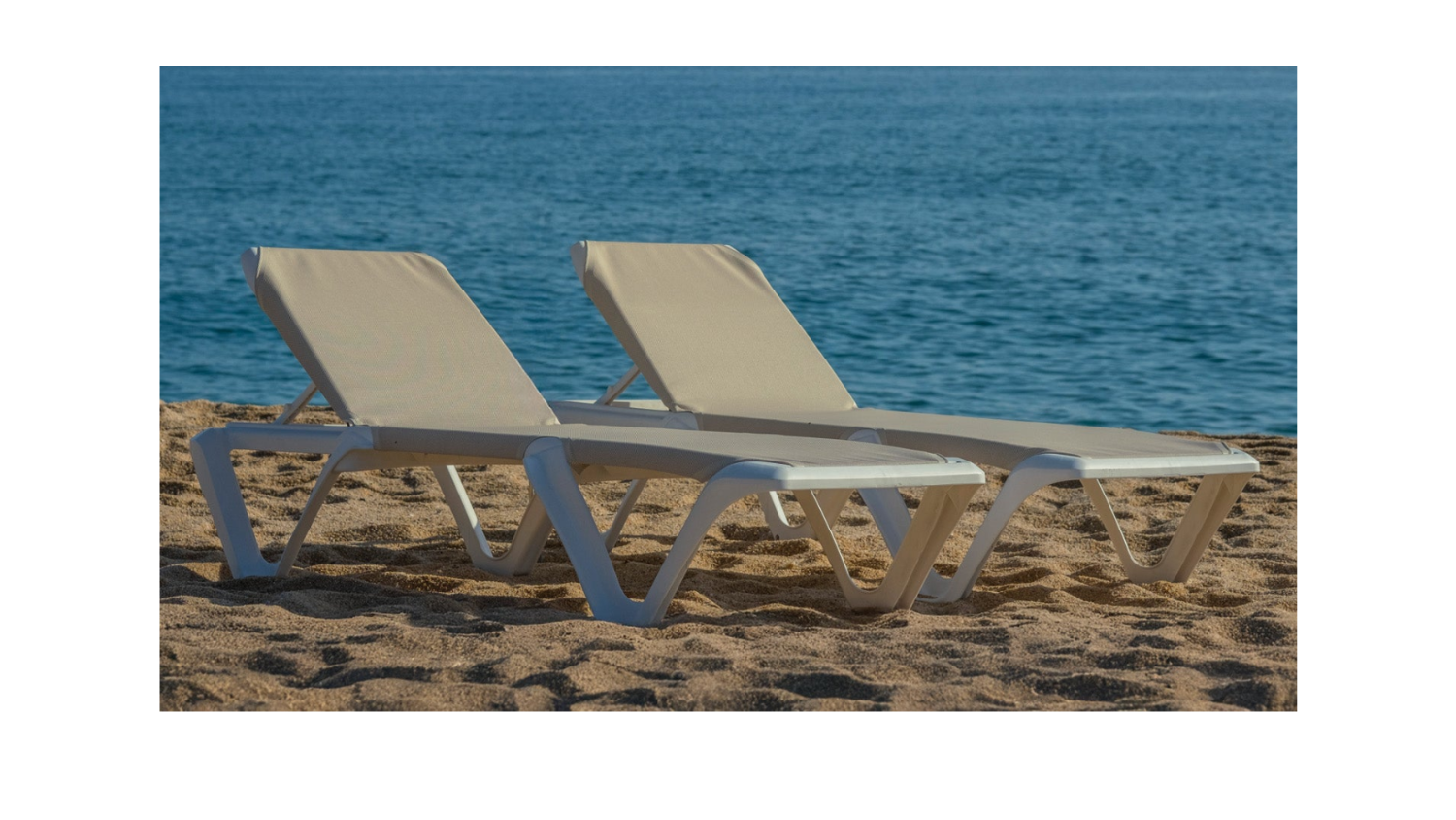 Two Chaise Lounges on a beach overlooking the ocean with a sunset on the horizon