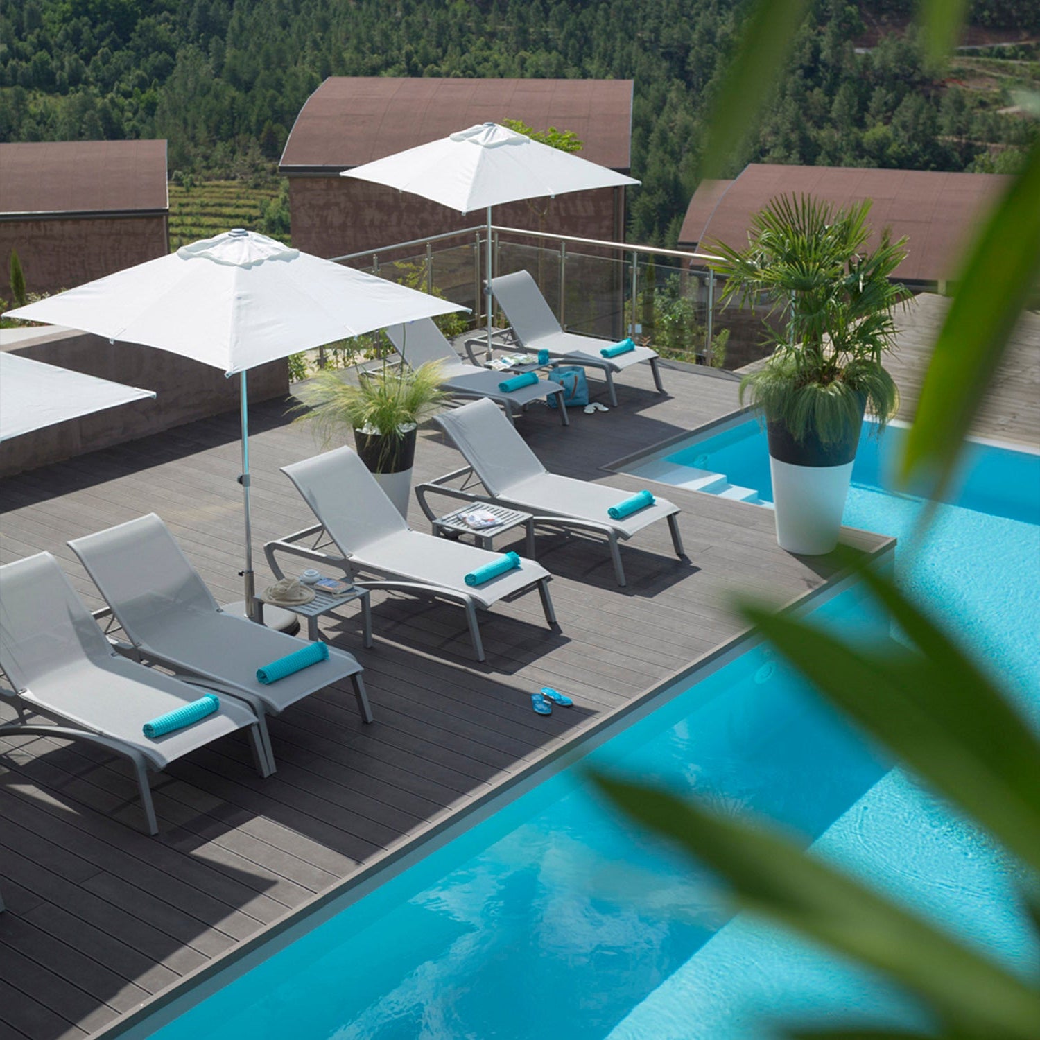 Poolside area with chaise lounges, umbrellas, and a view of the surrounding landscape.
